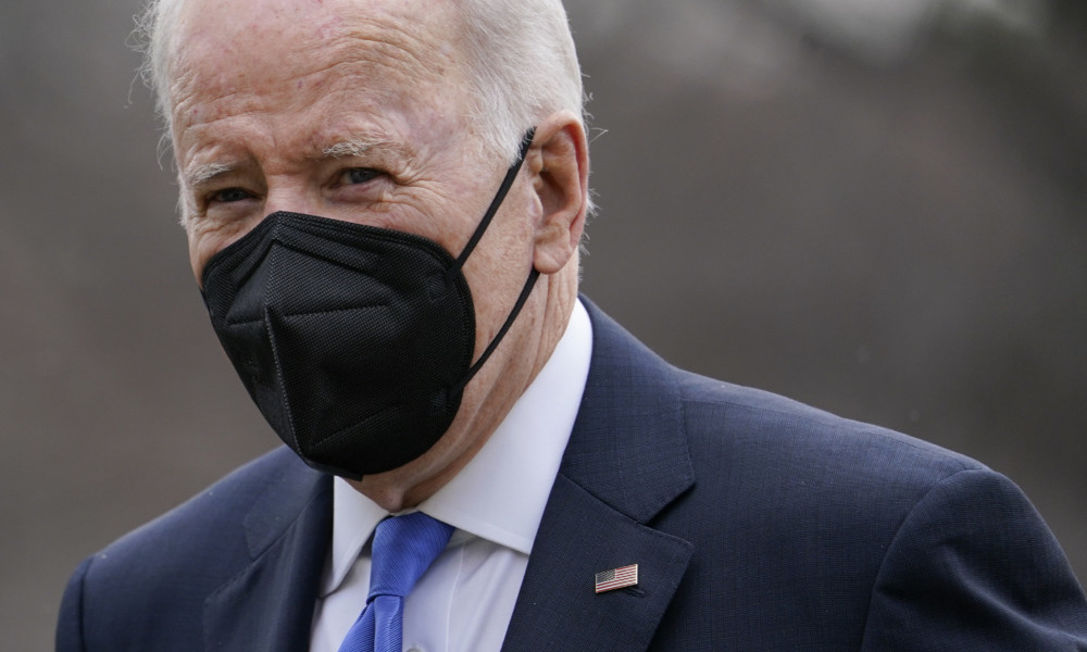 White House Protest: President Biden, closeup of older white man with short gray hair wearng black facemask and navy blue suit with white shirt and light blue tie