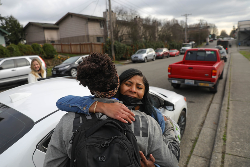 nonprofit homeless services: two adult women hug standing on sidewalk next a white car