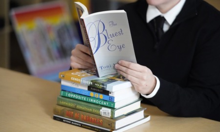 Activism grows in response to school book bans: person reading book atop stack of other books