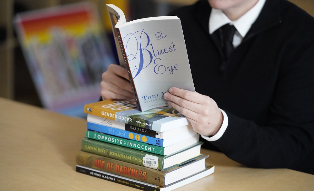 Activism grows in response to school book bans: person reading book atop stack of other books