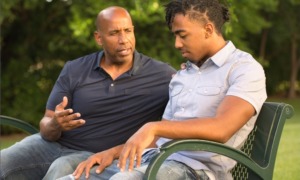mentoring for at-risk youth: older bald black man talks to young man on park bench