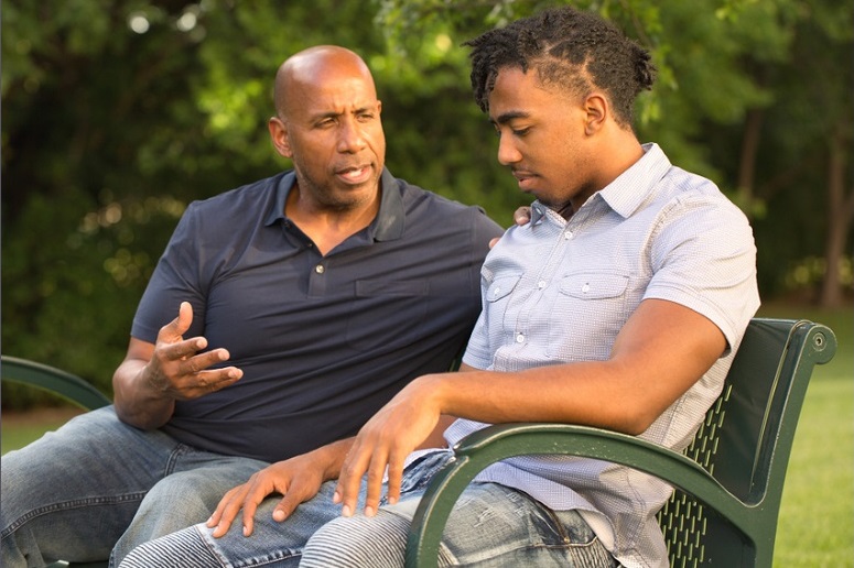 mentoring for at-risk youth: older bald black man talks to young man on park bench