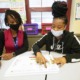 Detroit schools and federal aid: teacher and student work together at table with facemasks on
