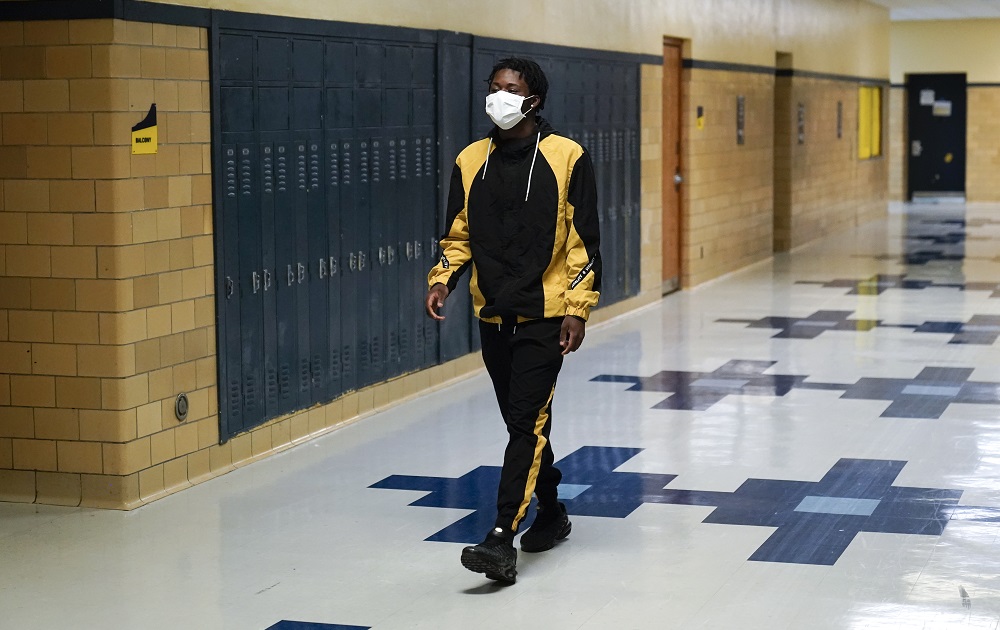 Detroit schools and federal aid: young black male student with facemask on walks down school hallway