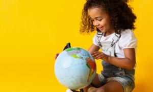 child development, early childhood grants: young girl looking at globe with yellow background