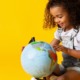 early childhood grants: young girl looking at globe with yellow background