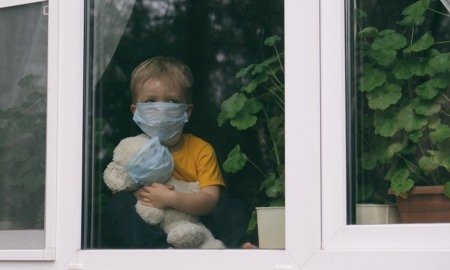 COVID orphan report: sad child in facemask with stuffed animal looks out window