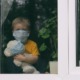 COVID orphan report: sad child in facemask with stuffed animal looks out window