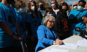 New Mexico offers equal pay to Native American teachers: older woman surrounded by people in matching blue Native logo shirts signing a document
