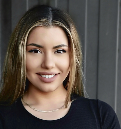 Trauma-informed: Jordan Costa headshot - Young woman with long brown hair wearing black top smiles into camera