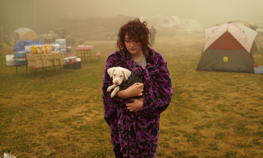 UN climate report: young woman holds her dog while wrapped in blanket while at temporary camp