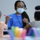 understaffing at after-school programs leaves unmet demand: black woman with long hair with facemask on works at a table with children