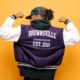Brooklyn youth grants: Black youth on solid brightly colored background in jacket flexing arms