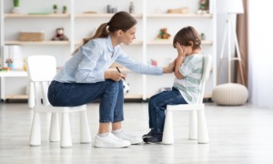 Early childhood mental health grants: young woman therapist comforts a crying young boy sitting on small white chairs