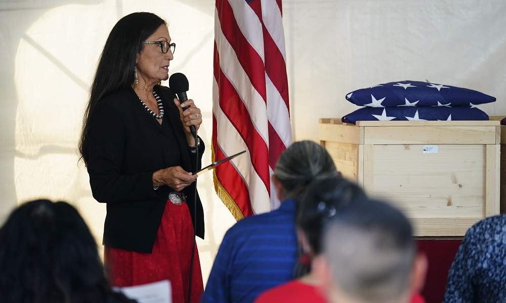 US church boarding school pasts: Native woman with microphone giving speech in front of audience