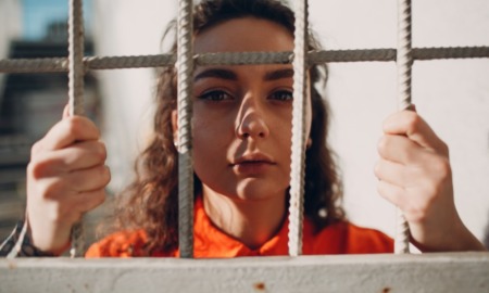 girls in juvenile justice support grants: young brunette girl in orange detention garb looking at camera from behind bars