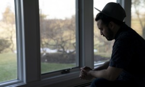 Dance company sex abuse: sad man in hat looking down in front of window in shadow