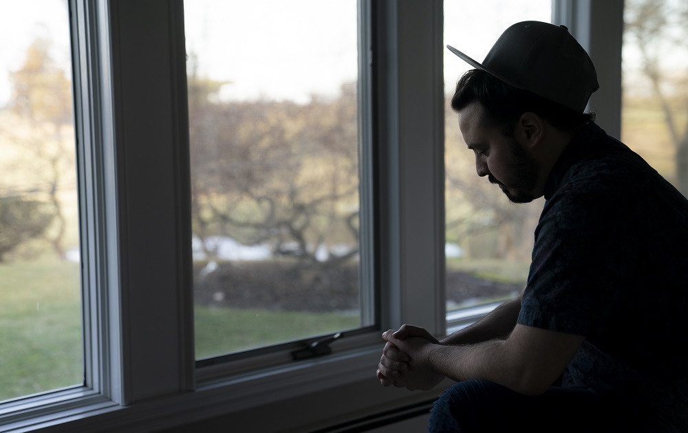 Dance company sex abuse: sad man in hat looking down in front of window in shadow