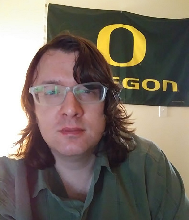 Missouri boarding school abuse: young man with long hair and glasses in front of Oregon university flag