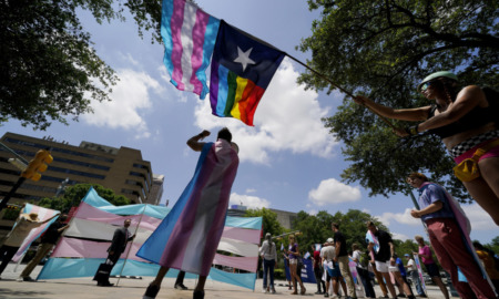 Texas transgender: Group of adults stand outside under a blue sky and waving flags.