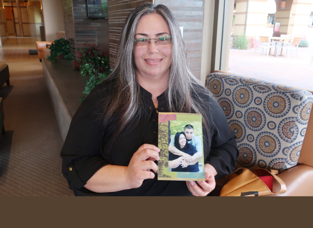 Juvenile lifers: Middle-aged woman with long dark, graying hair wearing black top stands holding collaged photo of her younger self with a young, dark-haired mn hugging her from the back