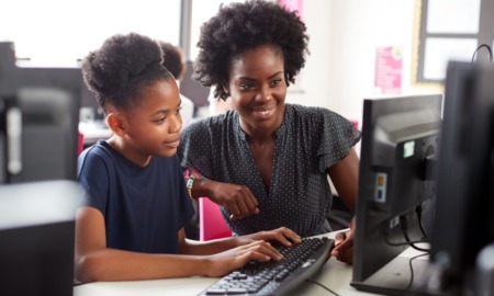 STEM education equity grants: Black female teacher helping a young black female student on computer