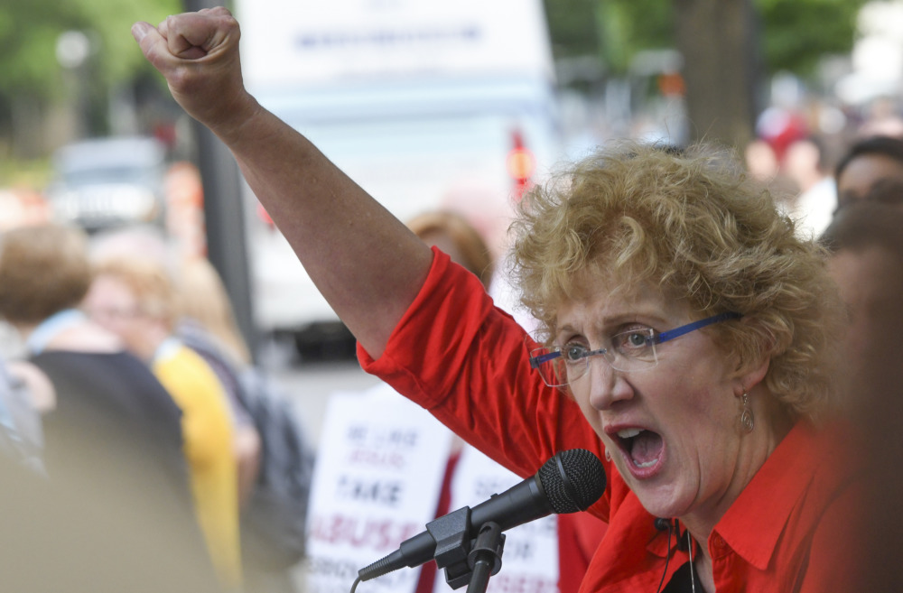 Southern Baptist sexual abuse investigative report: Middle-age woman with short, curly, blonde hair wearing red top holds up right fist while speaking into microphone.