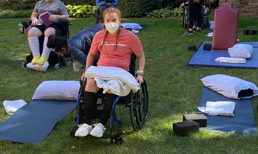 adaptive yoga: young woman in wheelchair surrounded by yoga mats and equipment