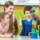 child care research grants: young, female child care professional with three young kids building blocks