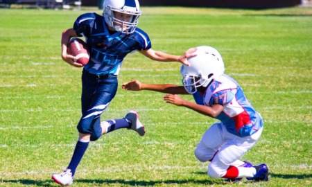 youth football field support grants: youth football player running with ball stiff-arming opposing player