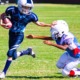 youth football field support grants: youth football player running with ball stiff-arming opposing player