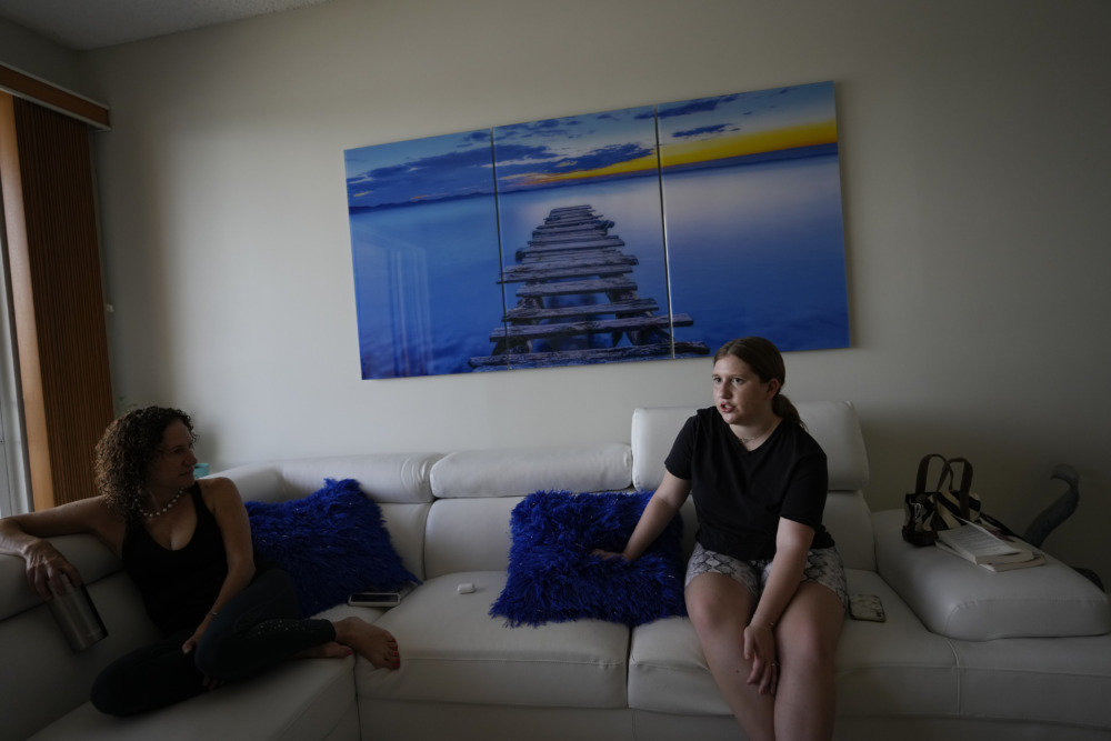 Parkland shooting survivor mental health: Young woman and middle aged woman sit on white couch with large blue ocean art on wall above couch.