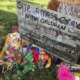 Native American Boarding School Deaths: Handprinted sign saying "Site mass graves native children,"sits amidst flowers