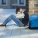 school violence prevention grants: young boy sitting against brick wall in hallway with hands on head and backpack on ground