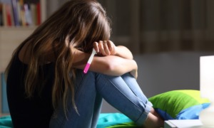 teen pregnancy prevention grants: sad teen on bed with head down holding a pregnancy test