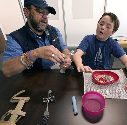 young caregivers offer crucial help: man in hat showing child silverware and eating methods for people with ALS