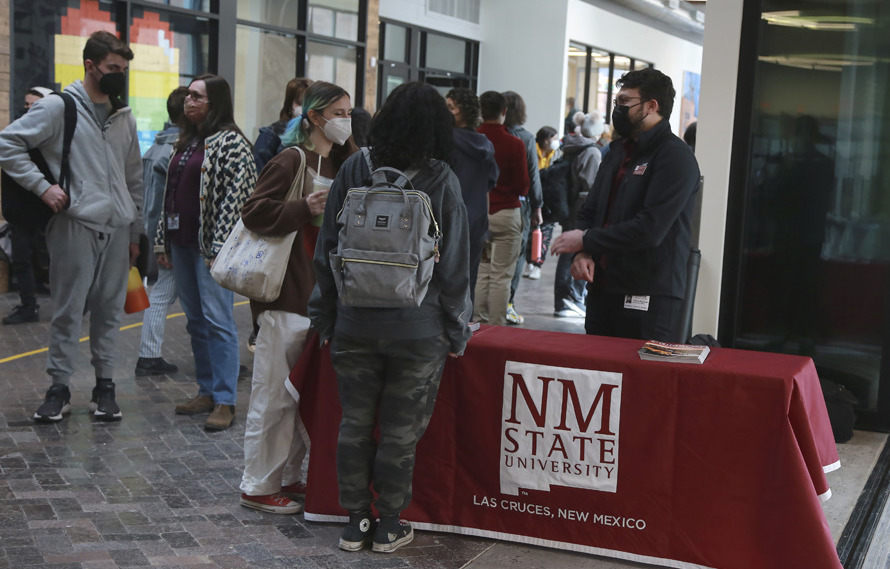 People stand around a table with a red NM State University covering