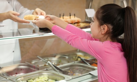 free school meals ending: young girl in pink shirt gets food from cafeteria worker