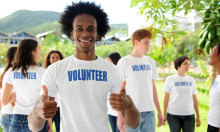 alternatives to youth incarceration grants: happy young black man in volunteer shirt giving thumps up with other youth volunteers in background