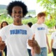 alternatives to youth incarceration grants: happy young black man in volunteer shirt giving thumps up with other youth volunteers in background