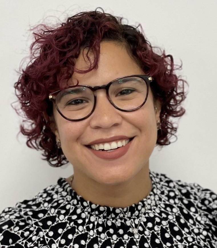 LGBTQ juvenile justice: Headshot of woman with sort, curly auburn hair with darkframed glasses wearing a black and white print top.