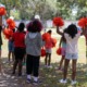 YMCA summer program: Several children in red t-sirts with red pompoms in the air stand facing a grassy field with backs to camera