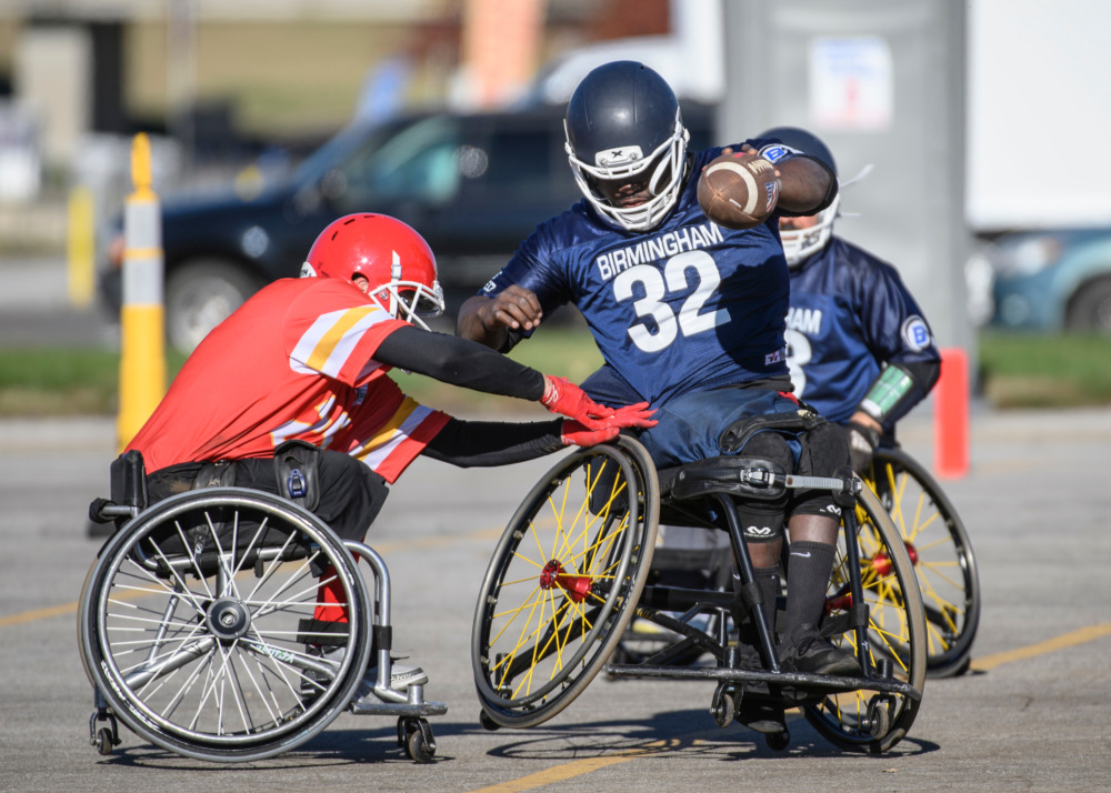 Wheelchair football: Several players from two teams in wheelchairs wearing team shirts and helmets try to block each other