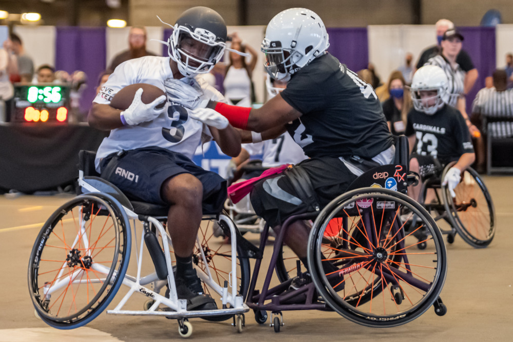 Wheelchair football: Several players from two teams in wheelchairs wearing team shirts and helmets try to block each other