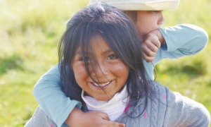 Native child care and foster care services grants: young native child with sibling on back smiling