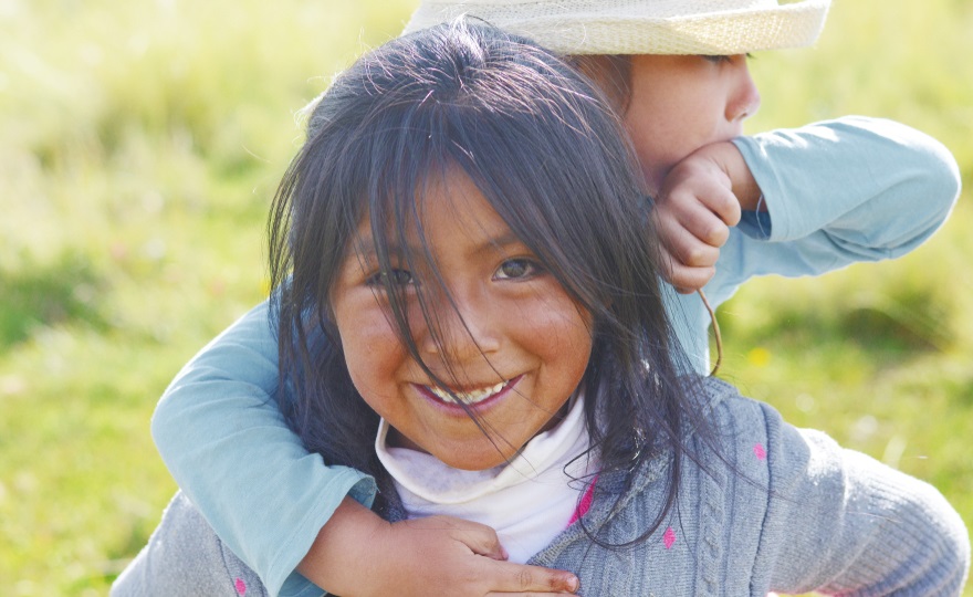 Native community child care and foster care services grants: young native child with sibling on back smiling