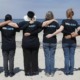 STEM education, hunger and community grants: people stand linking arms in chain on beach with shirts that say "we care"