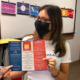 National Youth Leadership Council: Young dark-haired woman wearing pirnted face mask holds red. white and blue brochure up to camera