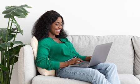 At-risk and foster youth transitional living grants: happy young Black woman on couch with laptop