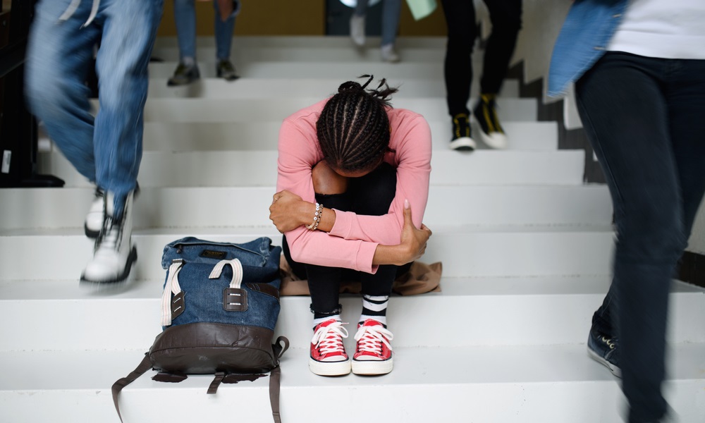 Mental health: young black girl sitting on school steps with head lowered and hugging her legs
